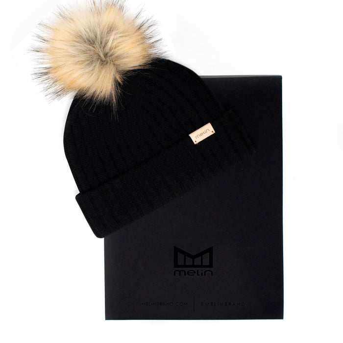The frontal view of the Melin All-Day Pom Beanie in black next to packaging
