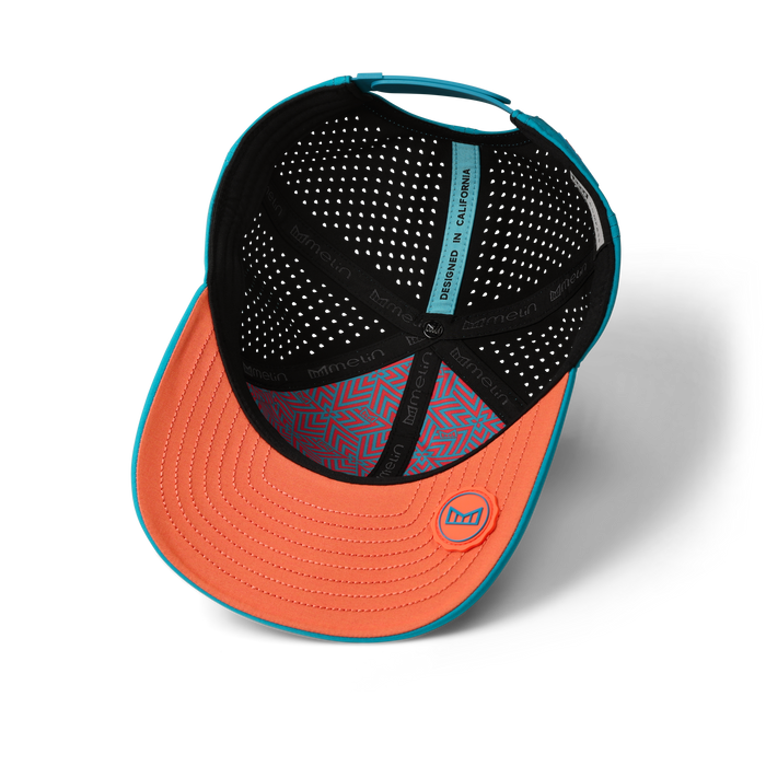 Baseball cap with orange bill, teal trim, perforated black interior, and geometric patterned sweatband.