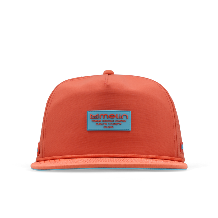 Hot coral snapback cap with blue rectangular patch label and blue bill trim.