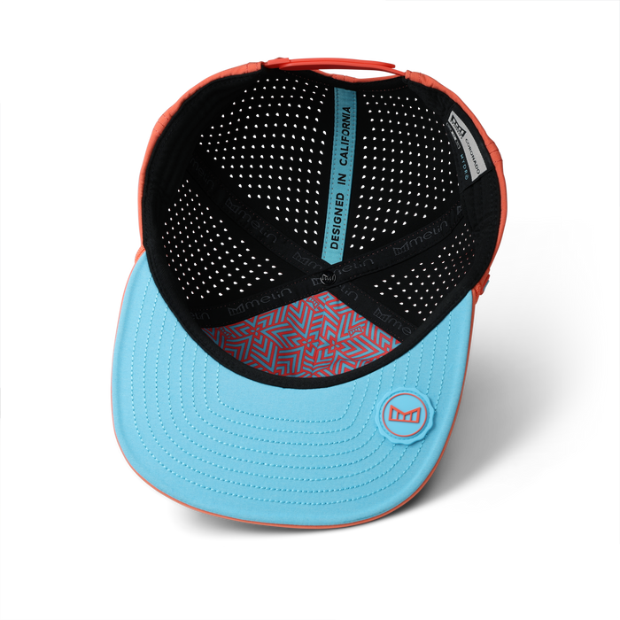 Hot coral and light blue baseball cap with perforated black interior and geometric patterned sweatband.
