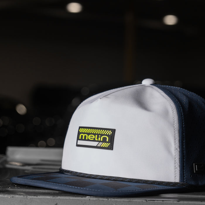 Black Iris and white colorblock snapback cap with yellow Melin brand logo patch on front panel.