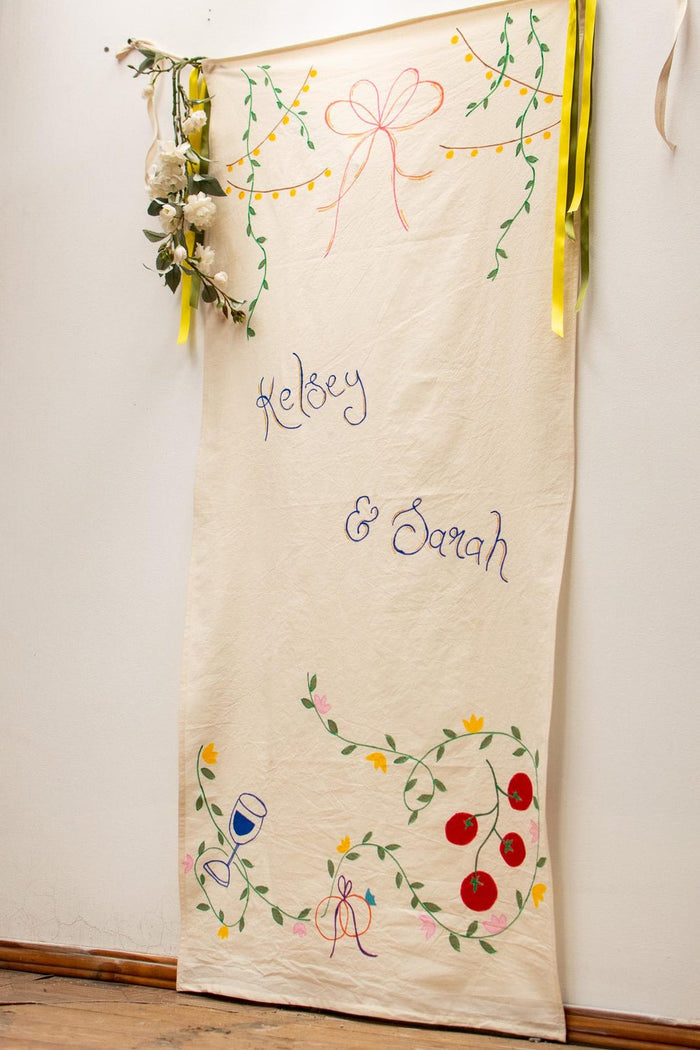 Hand-painted wedding banner with couple names in blue script, floral vines and string lights