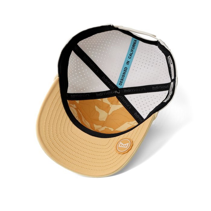 Tan baseball cap with black rope trim, white mesh back panel, orange patterned interior, and blue design label.
