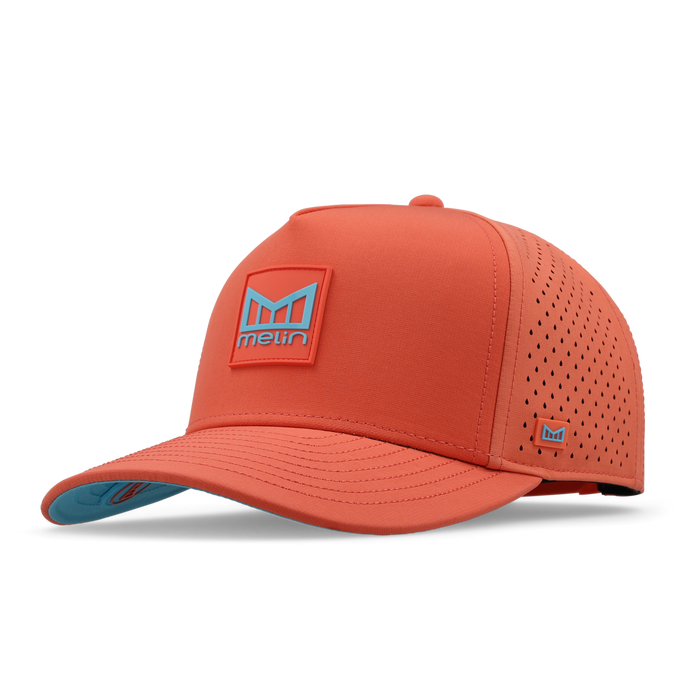 Hot coral baseball cap with perforated panels, blue logo patch on front, and teal undervisor.