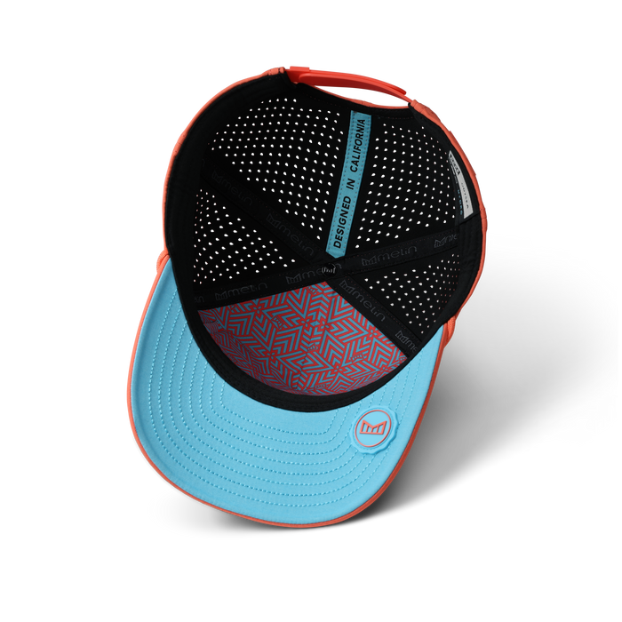 Hot coral and light blue baseball cap with perforated black interior and geometric patterned sweatband.