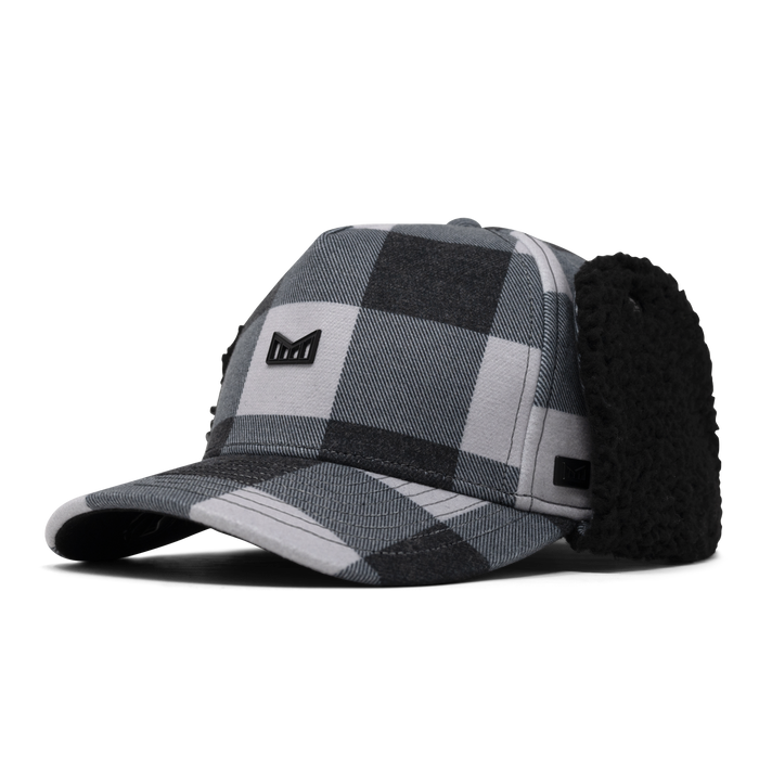 Black and white plaid thermal cap with attached black fleece ear warmers and small brand logo patch.