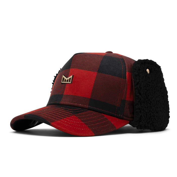 Red and black buffalo plaid baseball cap with black fleece ear flaps and gold metal logo badge.