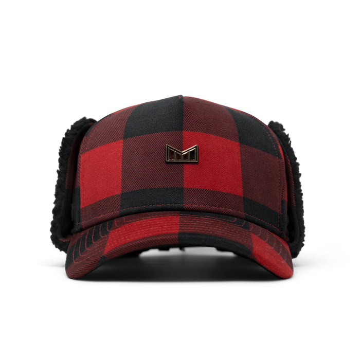 Red and black buffalo plaid thermal cap with black fleece ear flaps and metal logo badge.