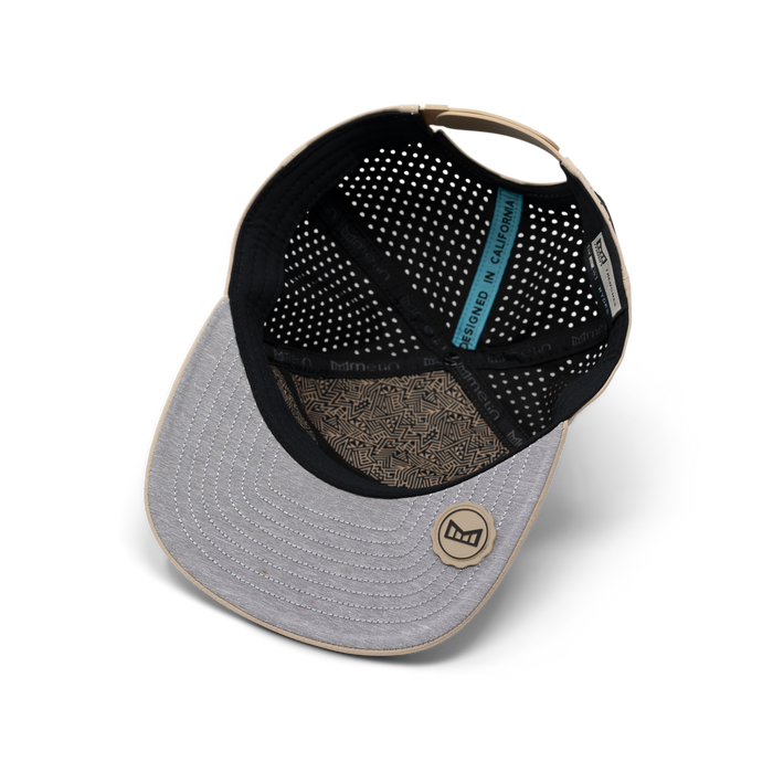 Khaki baseball cap with black mesh interior, tan trim, circular logo on front, and blue label visible inside.