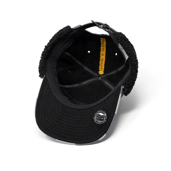 Black baseball cap with white side panels, black fleece ear warmers, and circular logo patch on front.
