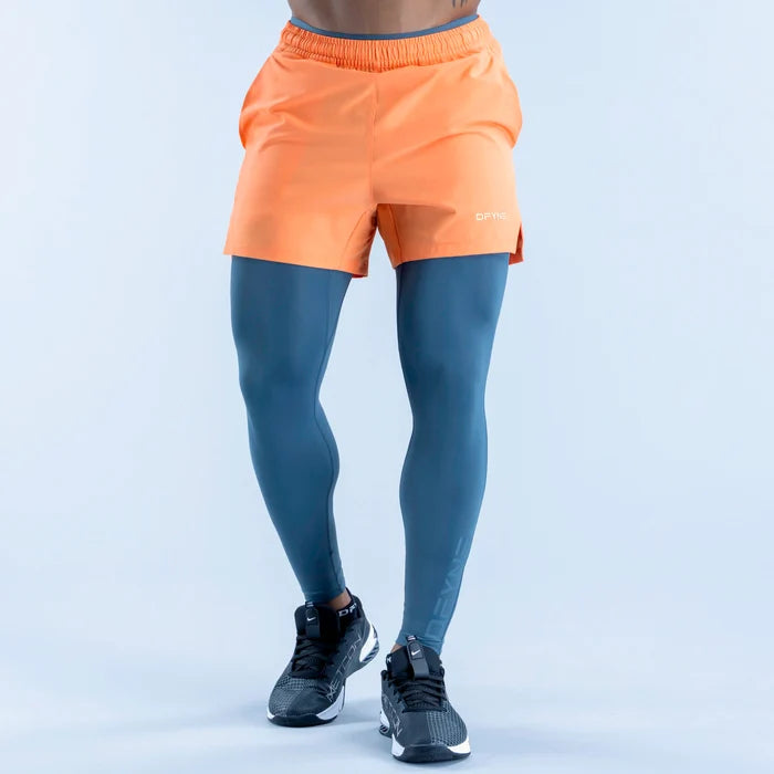 Orange shorts over teal-blue baselayer leggings with elastic waistband and seams.